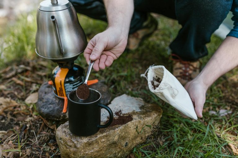 Person Holding Stainless Steel Teapot Pouring Black Ceramic Mug